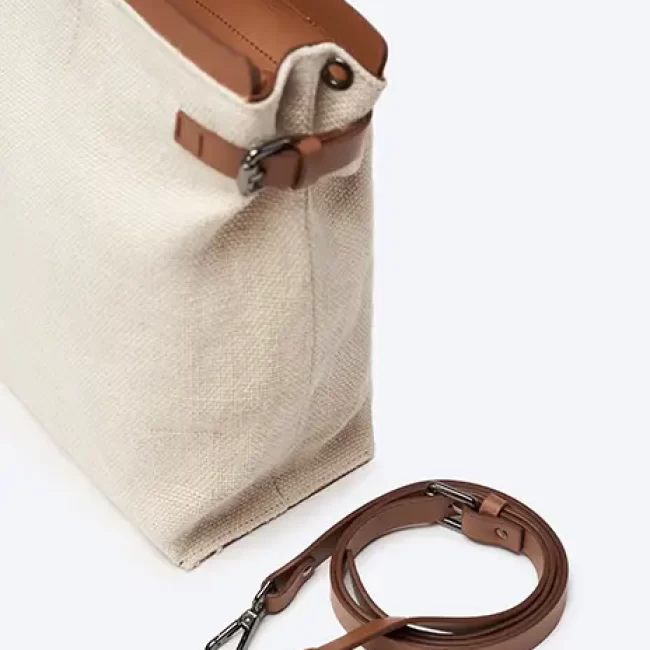 Bolso beige con detalles en cuero marrón y correa ajustable