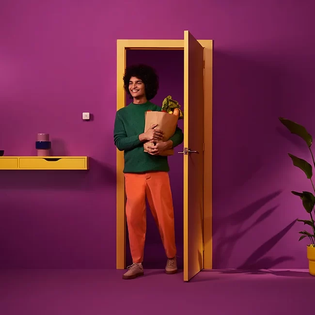 Persona entrando a una habitación con paredes púrpuras, llevando una bolsa de compras